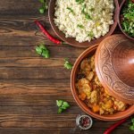 Traditional tajine dishes, couscous and fresh salad on rustic wooden table